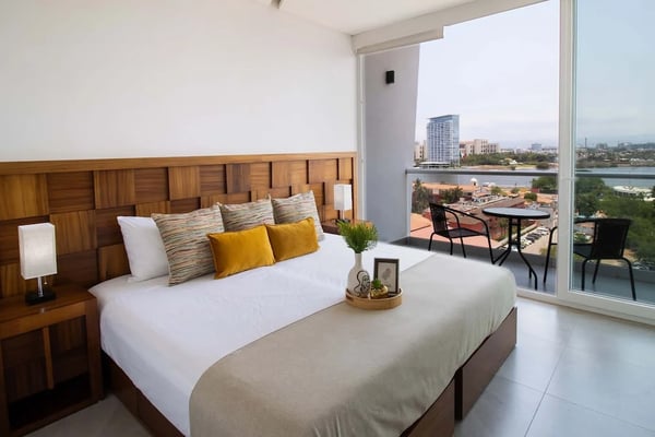 Rooftop pool deck with lounge chairs, umbrellas, and ocean view overlooking high-rise building