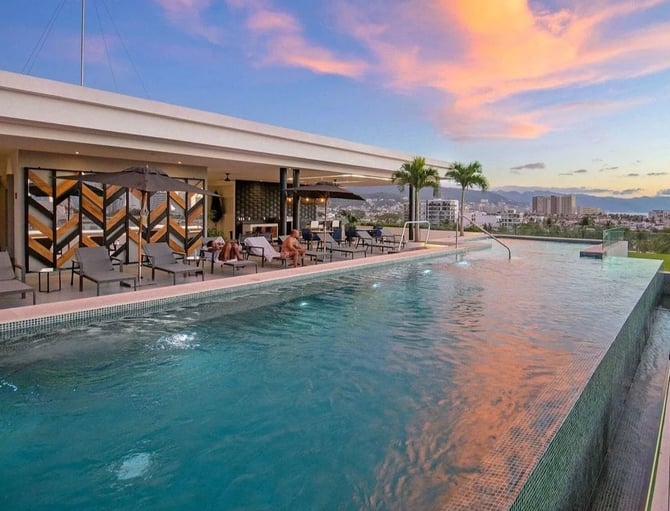 Rooftop pool and lounge area with city and ocean views at sunset